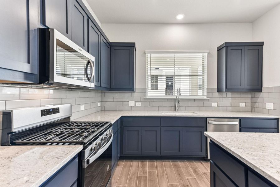 Kitchen featuring appliances with stainless steel finishes, light stone counters, wood tiled floors, tasteful backsplash, and recessed lighting Kitchen featuring appliances with stainless steel finishes, light stone counters, wood tiled floors, tasteful backsplash, and recessed lighting