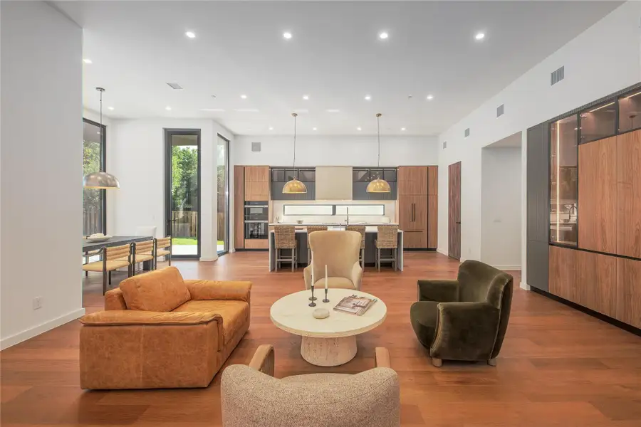 An open floorplan seamlessly connects the living area to a modern kitchen, featuring high ceilings and warm wood flooring.