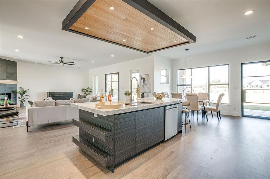 Kitchen with recessed lighting, a tiled fireplace, modern cabinets, and light wood-type flooring Kitchen with recessed lighting, a tiled fireplace, modern cabinets, and light wood-type flooring