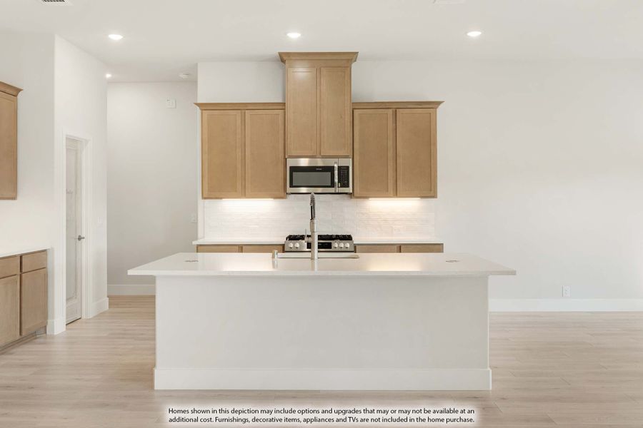 Kitchen with large white island, light wood cabinets, stainless steel microwave, and white tile backsplash Kitchen with large white island, light wood cabinets, stainless steel microwave, and white tile backsplash