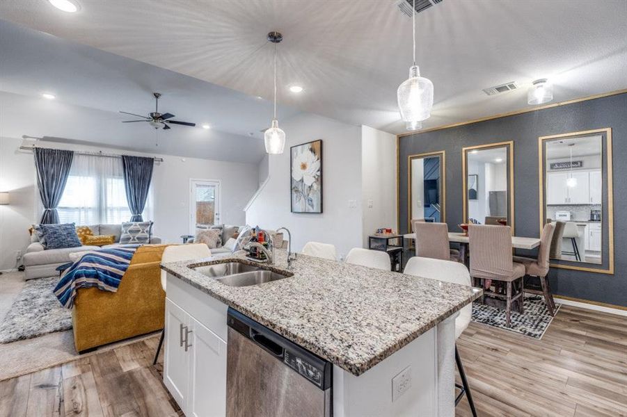 Kitchen with a breakfast bar, light stone countertops, stainless steel dishwasher, a center island with sink, and white cabinetry