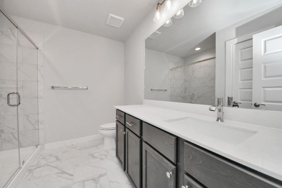 Secondary bath features tile flooring, walk-in shower with tile surround, light stained wood cabinets, beautiful light countertop.