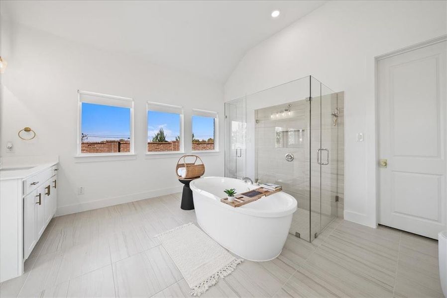 Bathroom with lofted ceiling, a soaking tub, vanity, a shower stall, and baseboards