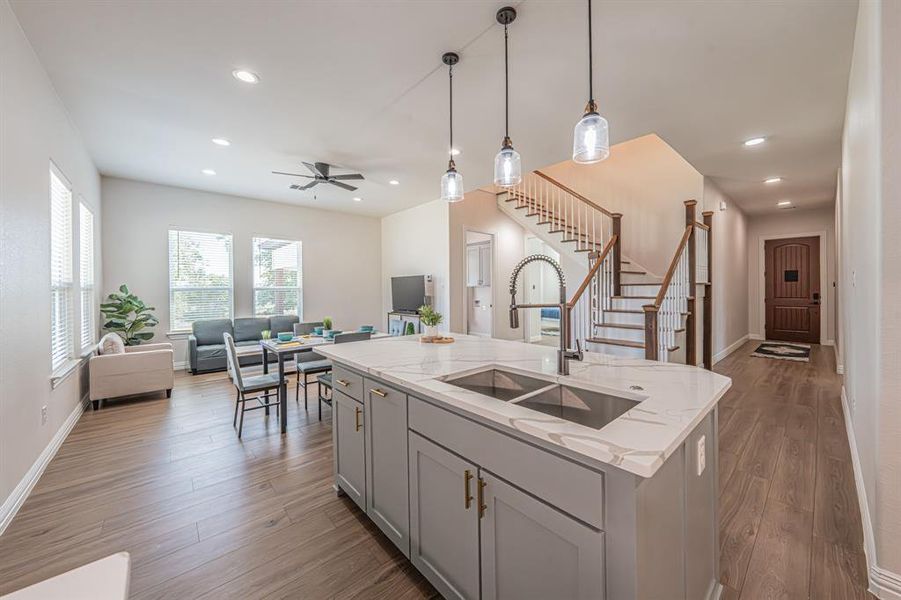 Kitchen featuring hanging light fixtures, open floor plan, light stone counters, light wood-style flooring, and a center island with sink Kitchen featuring hanging light fixtures, open floor plan, light stone counters, light wood-style flooring, and a center island with sink