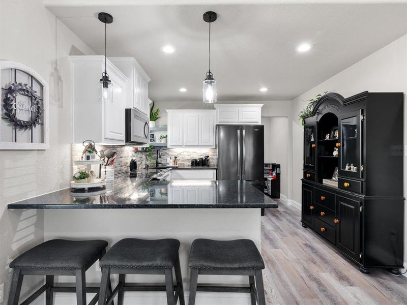 Kitchen with light wood finished floors, decorative backsplash, a peninsula, freestanding refrigerator, and white cabinets