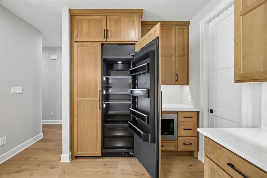 Kitchen featuring light wood-style floors, stainless steel microwave, tasteful backsplash, and light stone counters Kitchen featuring light wood-style floors, stainless steel microwave, tasteful backsplash, and light stone counters