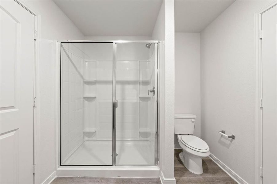 Bathroom with hardwood / wood-style flooring, toilet, and a shower with door