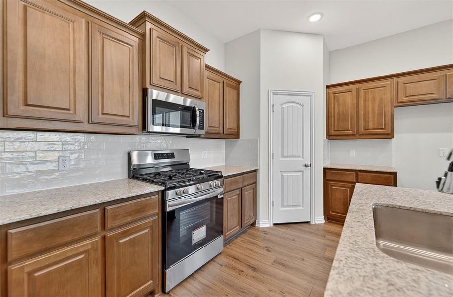 Kitchen featuring appliances with stainless steel finishes, brown cabinets, light stone counters, light wood-style flooring, and recessed lighting