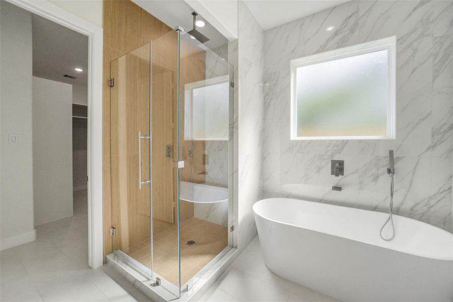This bathroom features a sleek, modern design with a freestanding bathtub, glass-enclosed shower, and elegant marble walls, creating a luxurious and spa-like atmosphere.