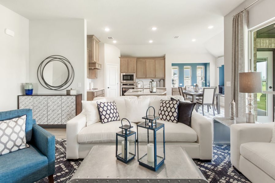 Open-concept living room with white sofa, blue accents, and kitchen visible in background