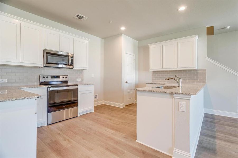Kitchen featuring white cabinetry, sink, stainless steel appliances, light stone countertops, and light wood-type flooring