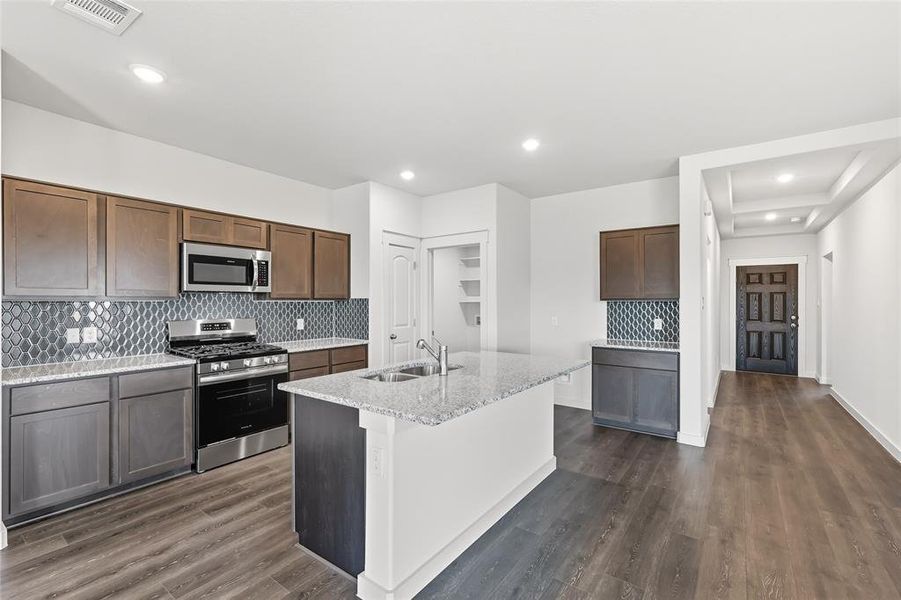 Kitchen featuring decorative backsplash, appliances with stainless steel finishes, light stone countertops, dark wood-style floors, and an island with sink Kitchen featuring decorative backsplash, appliances with stainless steel finishes, light stone countertops, dark wood-style floors, and an island with sink
