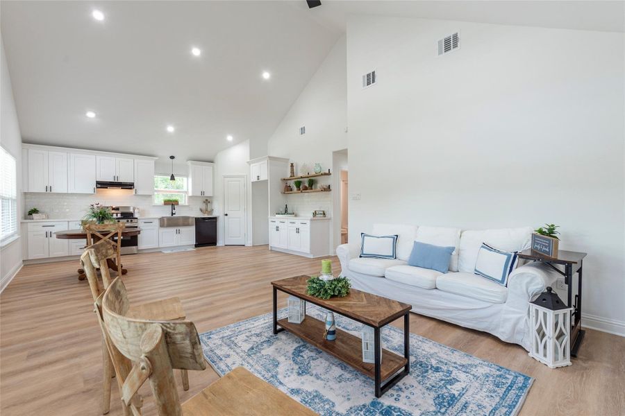 Spacious and open living room space with high ceilings, recessed can lighting, ceiling fan fixture and vinyl flooring.