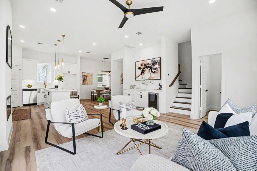 This photo showcases a modern, open-concept living area with sleek wood flooring and abundant natural light. The space features a stylish kitchen with white cabinetry and pendant lighting, a cozy sitting area with contemporary furnishings, and a staircase leading to the upper level. The layout is inviting and ideal for entertaining.