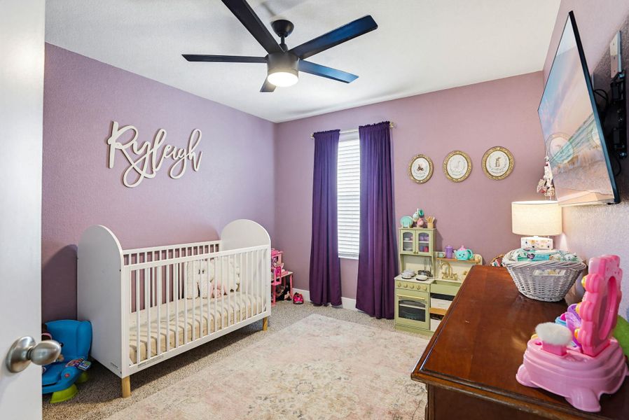 Carpeted room with a ceiling fan, window with blinds and purple drapes, and a wall-mounted television