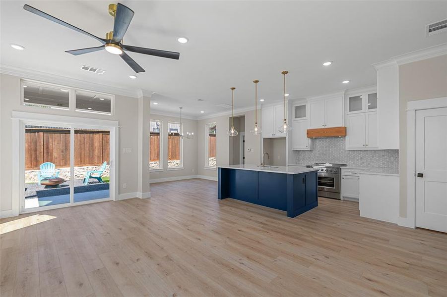 Kitchen with hanging light fixtures, white cabinets, ceiling fan with notable chandelier, light wood-type flooring, and high end range