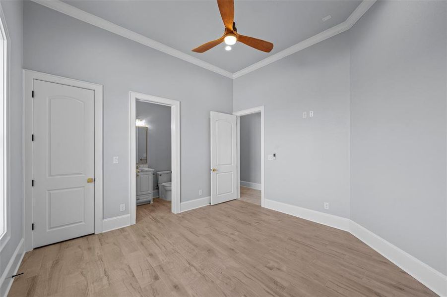 Unfurnished bedroom featuring light wood finished floors, crown molding, ensuite bathroom, and a ceiling fan Unfurnished bedroom featuring light wood finished floors, crown molding, ensuite bathroom, and a ceiling fan