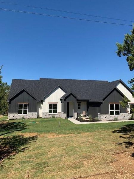 Modern farmhouse with a shingled roof, a front lawn, a porch, and board and batten siding Modern farmhouse with a shingled roof, a front lawn, a porch, and board and batten siding