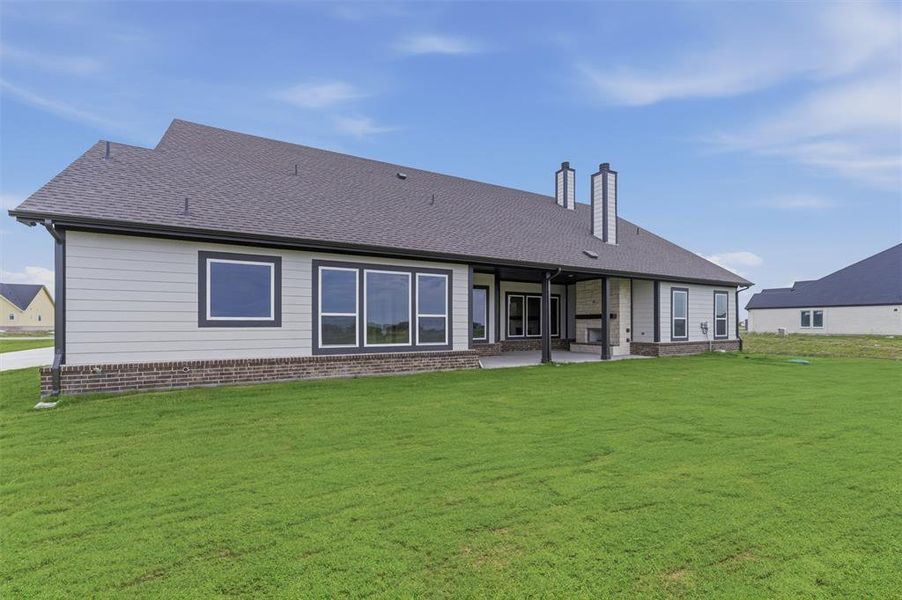 Expansive rear exterior featuring a covered patio, multiple large windows, and a dual-flue chimney system