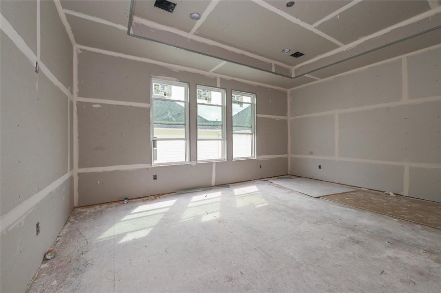 Primary bedroom with large windows and double tray ceilings