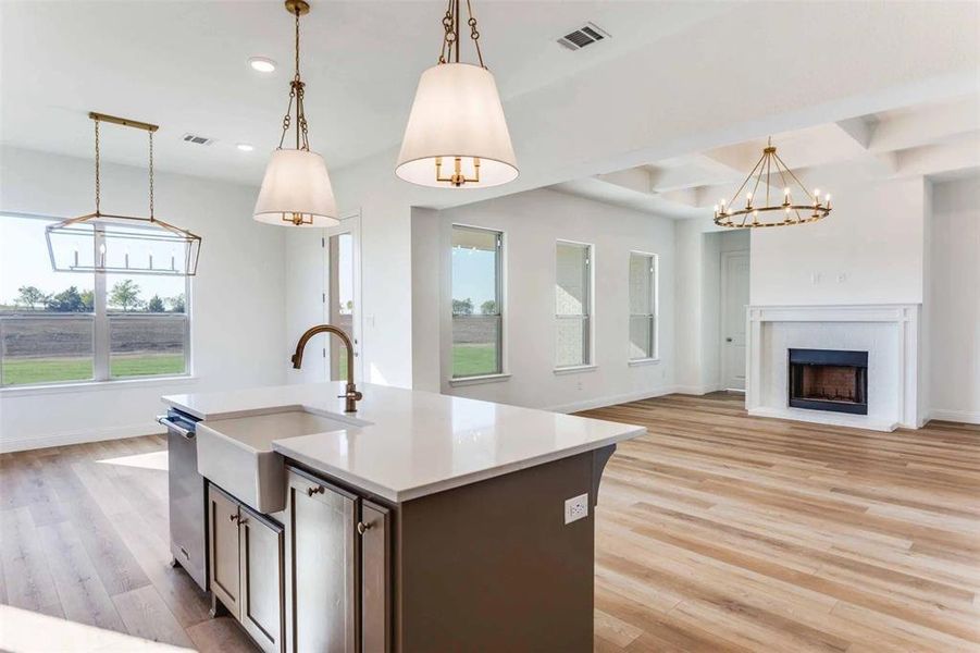 Kitchen with open floor plan, a chandelier, a center island with sink, light wood-type flooring, and a fireplace