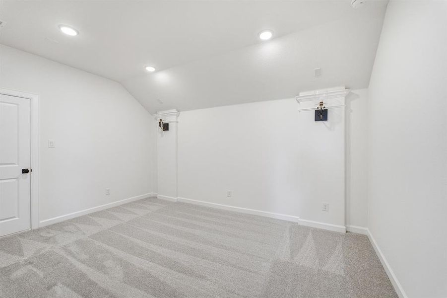 Spacious room featuring light gray patterned carpeting, recessed ceiling lighting, a white panel door with black hardware, and angled ceiling details