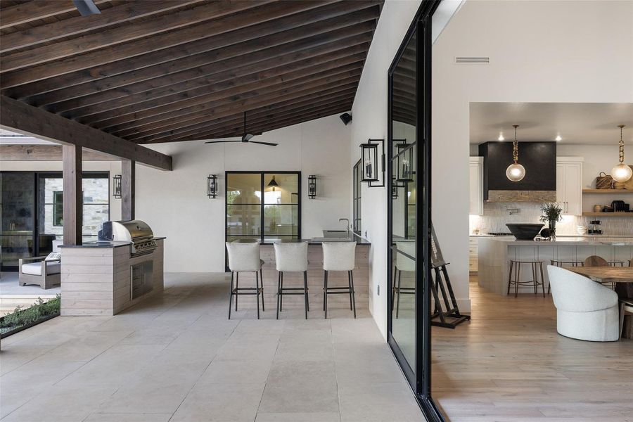 Optional To Be Built - An inviting outdoor living area features an exposed beam ceiling, a full kitchen with a built-in grill, and sliding glass doors.