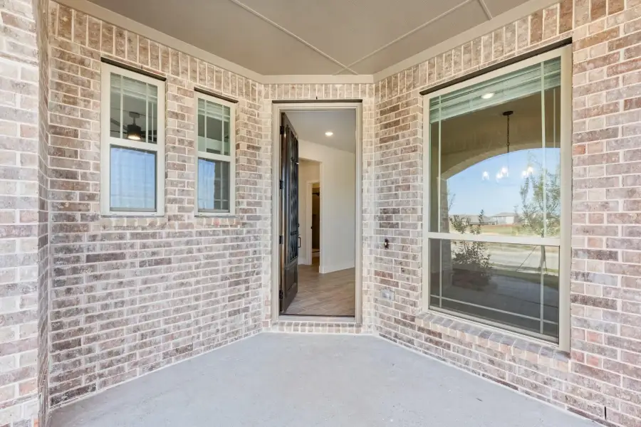 Covered front entry with brick exterior, open black door, and two large windows