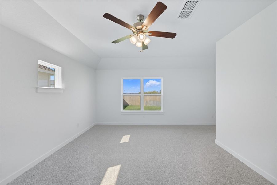 Carpeted empty room featuring lofted ceiling and a ceiling fan Carpeted empty room featuring lofted ceiling and a ceiling fan