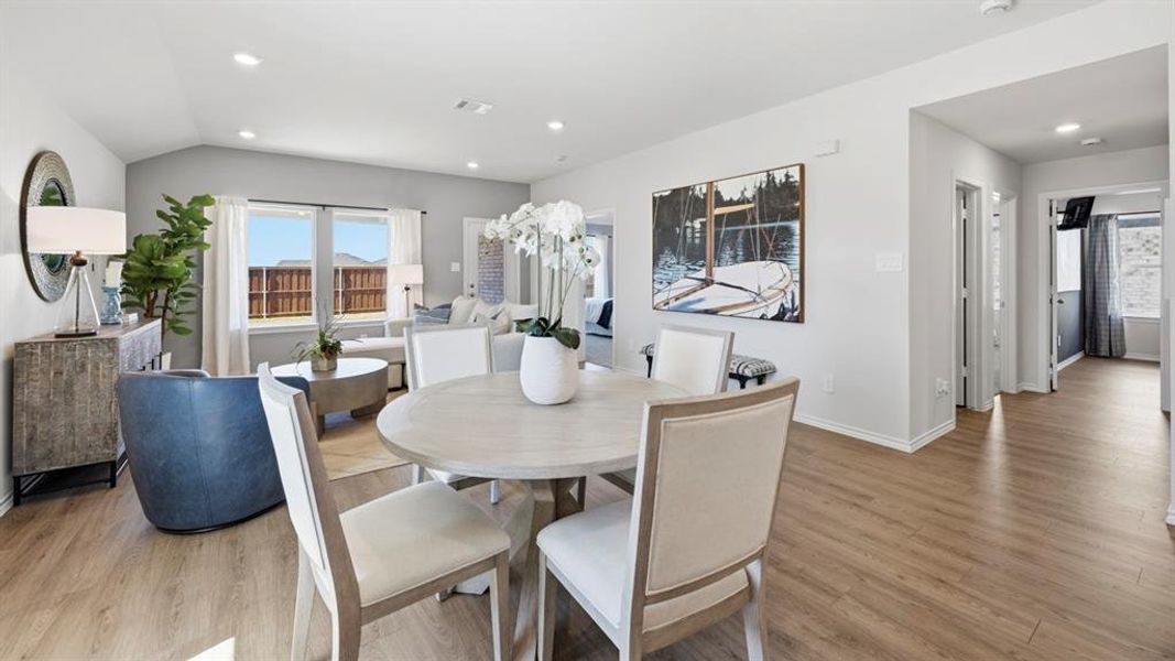 The open concept dining and living area features light-toned flooring and vaulted ceilings