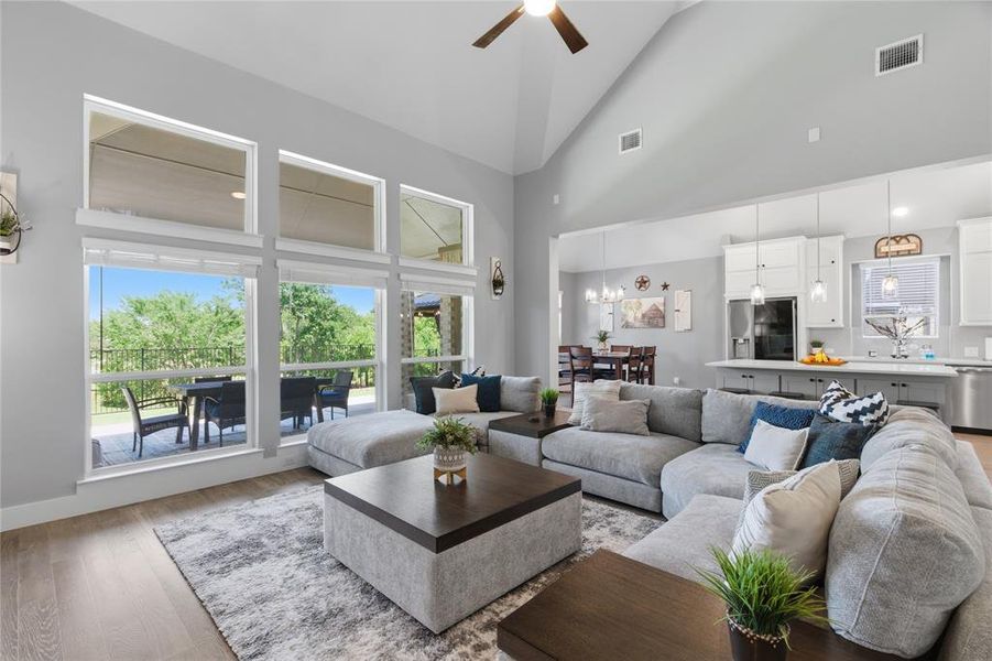 Great room featuring vaulted ceilings, wood-finish flooring, a contemporary ceiling fan, and a wall of windows overlooking an outdoor patio