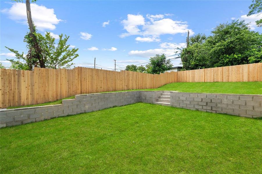 Terraced backyard with lush green lawn, concrete block retaining walls, and a light wood privacy fence