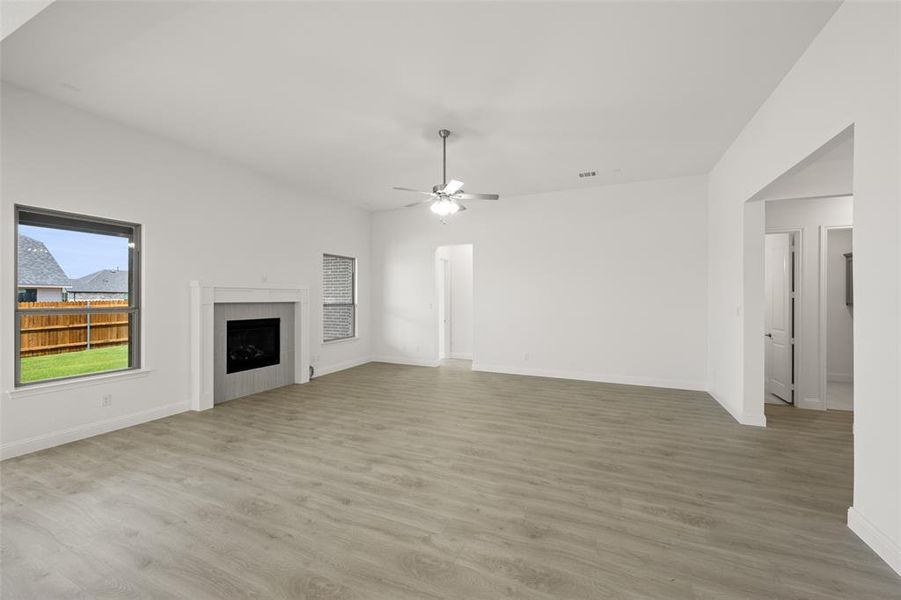 Unfurnished living room with light wood-style flooring, a ceiling fan, and a fireplace Unfurnished living room with light wood-style flooring, a ceiling fan, and a fireplace