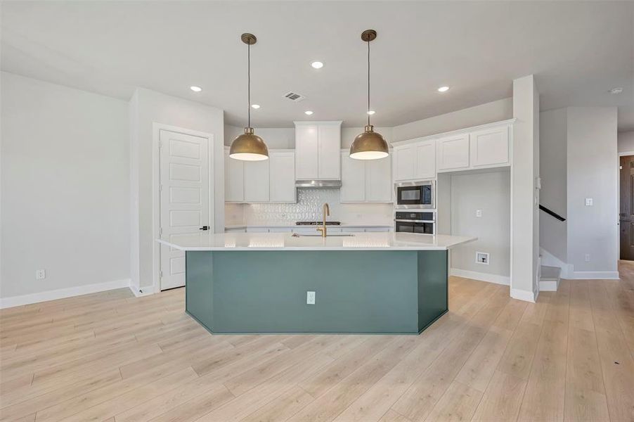 Kitchen with an island with sink, stainless steel appliances, light wood-style floors, pendant lighting, and two tone cabinetry Kitchen with an island with sink, stainless steel appliances, light wood-style floors, pendant lighting, and two tone cabinetry