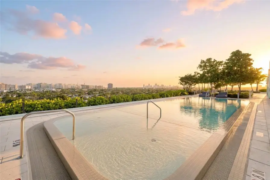 Rooftop swimming pool featuring a tiled deck, metallic handrails, and surrounding mature landscaping