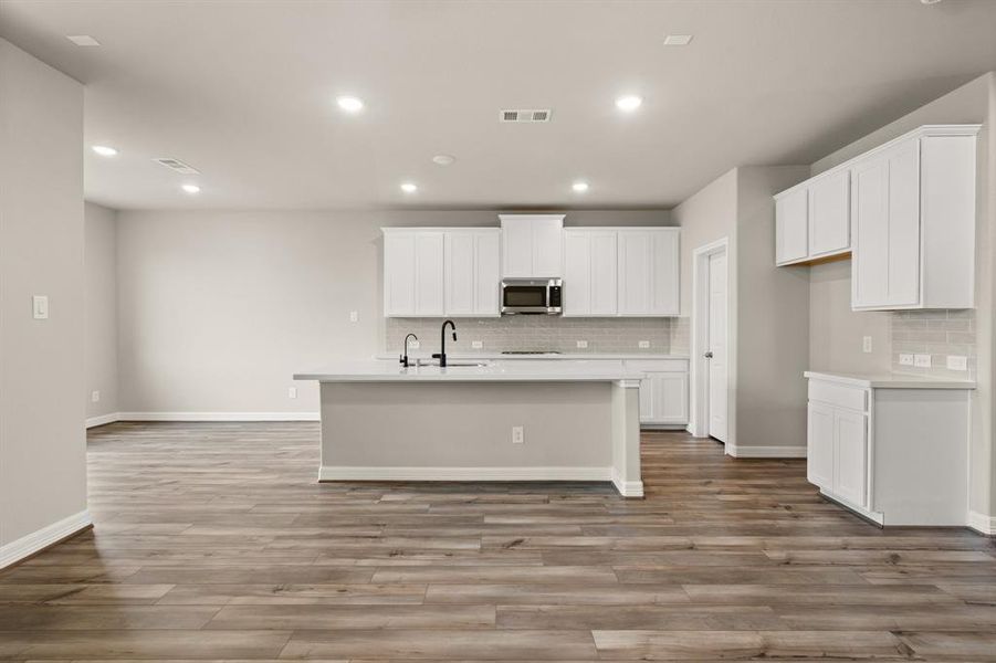 This light and bright kitchen features a large quartz island, white cabinets, a large sink overlooking your family room, recessed lighting, and beautiful backsplash.