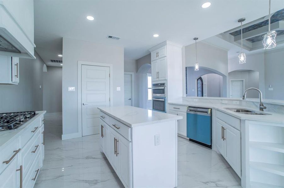 Kitchen featuring white cabinets, pendant lighting, a center island, appliances with stainless steel finishes, and light stone counters