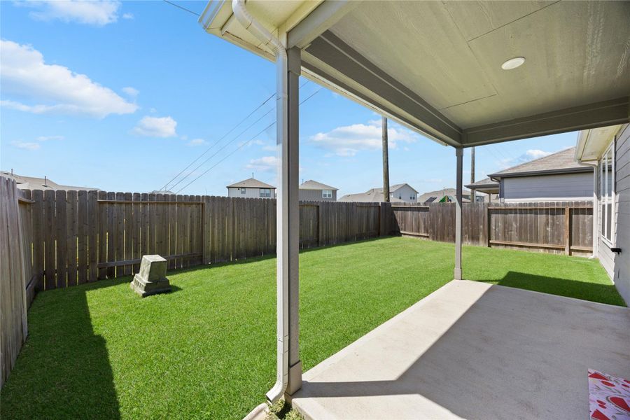 backyard with a well-maintained lawn, surrounded by a wooden privacy fence. There's a covered patio providing shade, making it ideal for outdoor relaxation.
