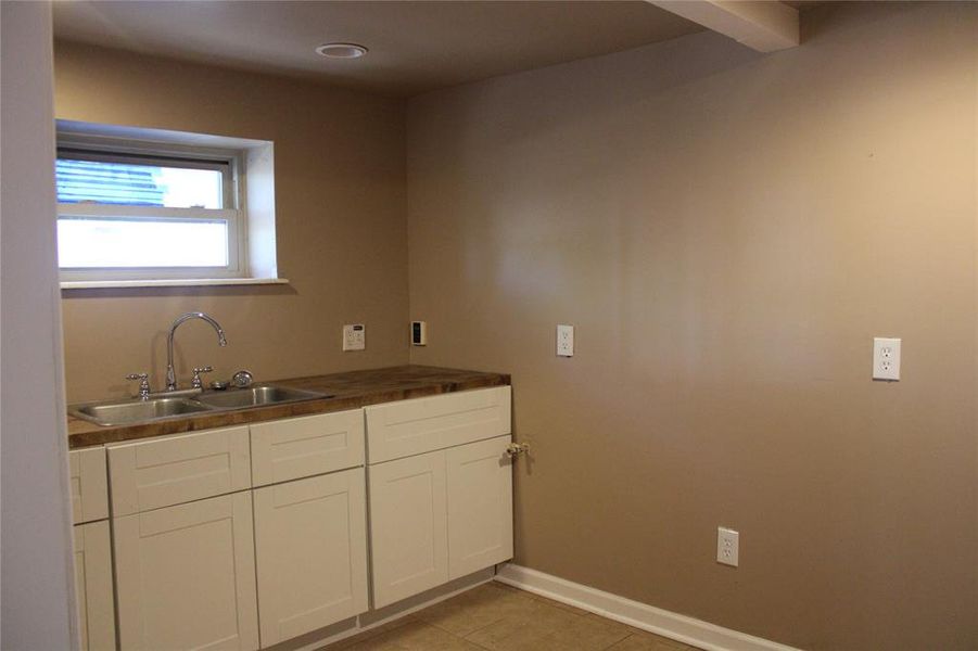Kitchen with white cabinets, light tile patterned floors, and wood counters Kitchen with white cabinets, light tile patterned floors, and wood counters