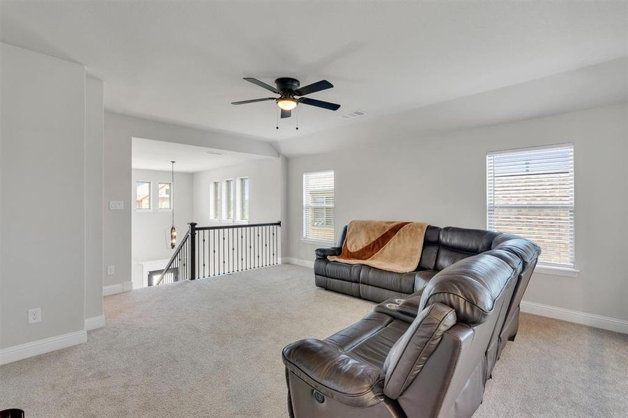 Spacious carpeted loft featuring a black ceiling fan, multiple windows with blinds, light gray wall paint, and white trim