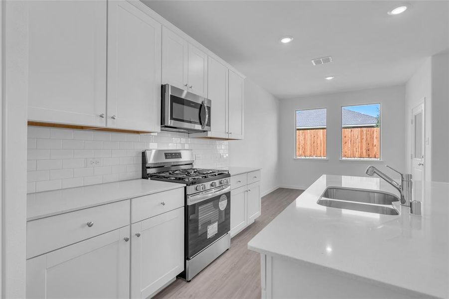 Kitchen with appliances with stainless steel finishes, white cabinetry, sink, and light hardwood / wood-style flooring