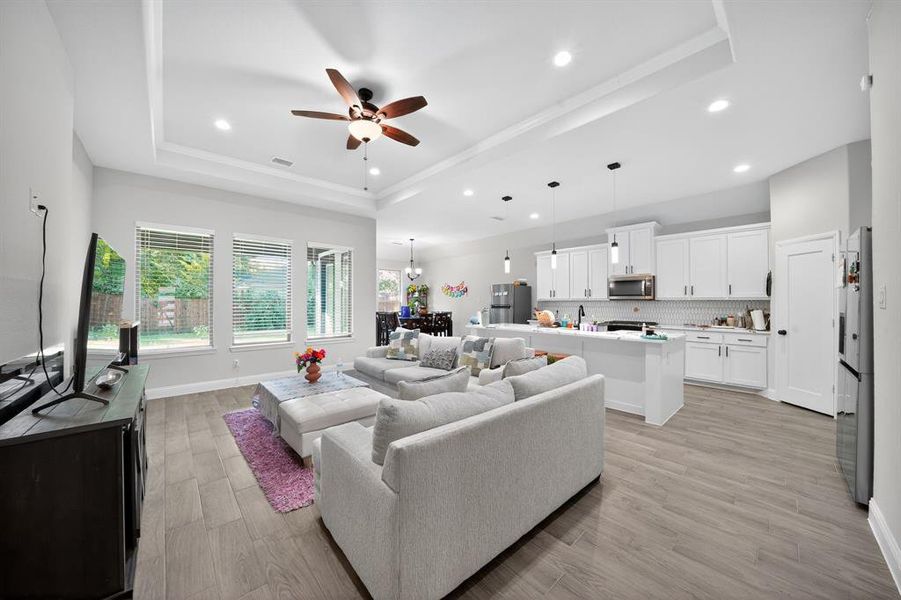 Living room featuring a tray ceiling, ceiling fan, light wood finished floors, recessed lighting, and a chandelier