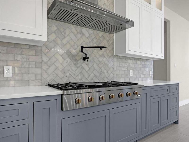 Kitchen with white cabinetry, wall chimney exhaust hood, stainless steel gas stovetop, and decorative backsplash