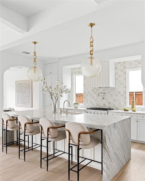 Kitchen with white cabinets, light stone countertops, a large island with sink, and pendant lighting