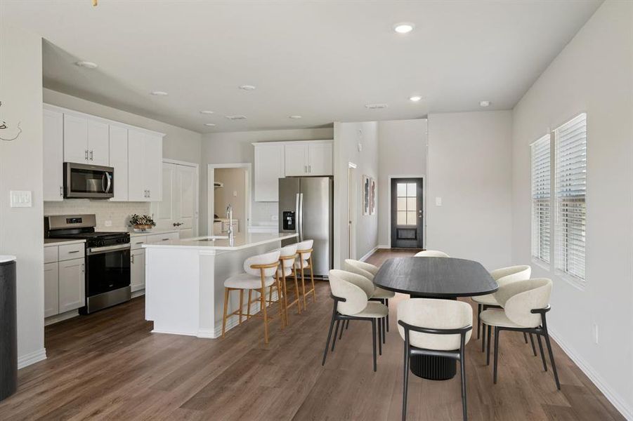 Kitchen with appliances with stainless steel finishes, a kitchen breakfast bar, white cabinetry, a center island with sink, and recessed lighting