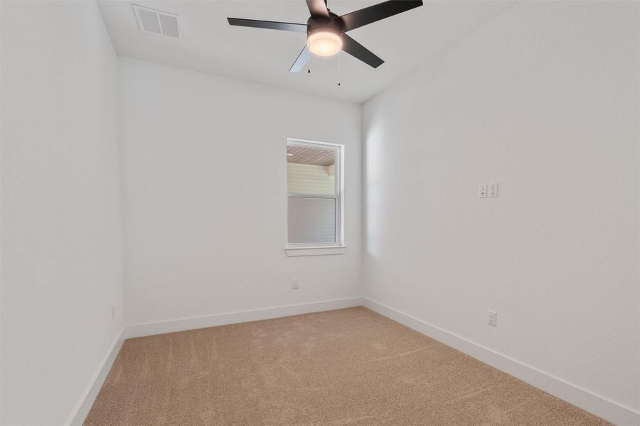 A well-lit bedroom features plush carpeting and a modern ceiling fan for year-round comfort.