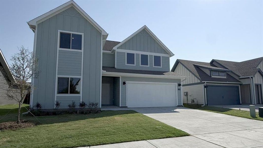 View of front of home with board and batten siding, an attached garage, driveway, and a front yard