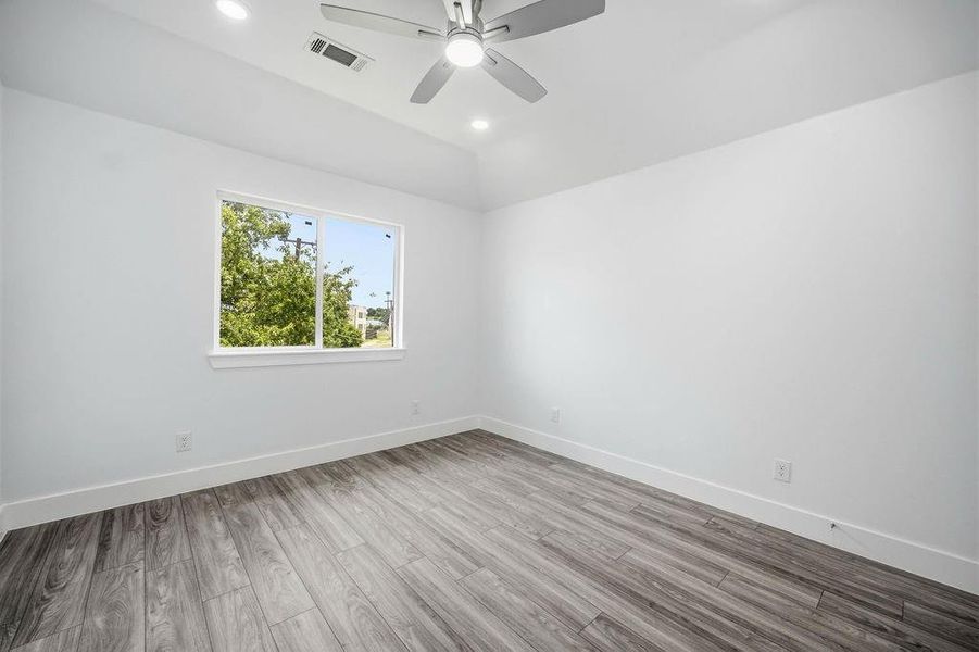 Bright room featuring wood-finish flooring, a contemporary ceiling fan with integrated lighting, recessed overhead lights, and a window providing natural illumination Bright room featuring wood-finish flooring, a contemporary ceiling fan with integrated lighting, recessed overhead lights, and a window providing natural illumination