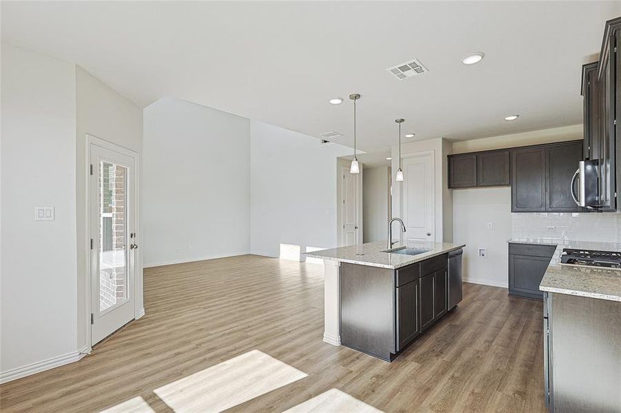 Kitchen with light hardwood / wood-style flooring, light stone countertops, and an island with sink