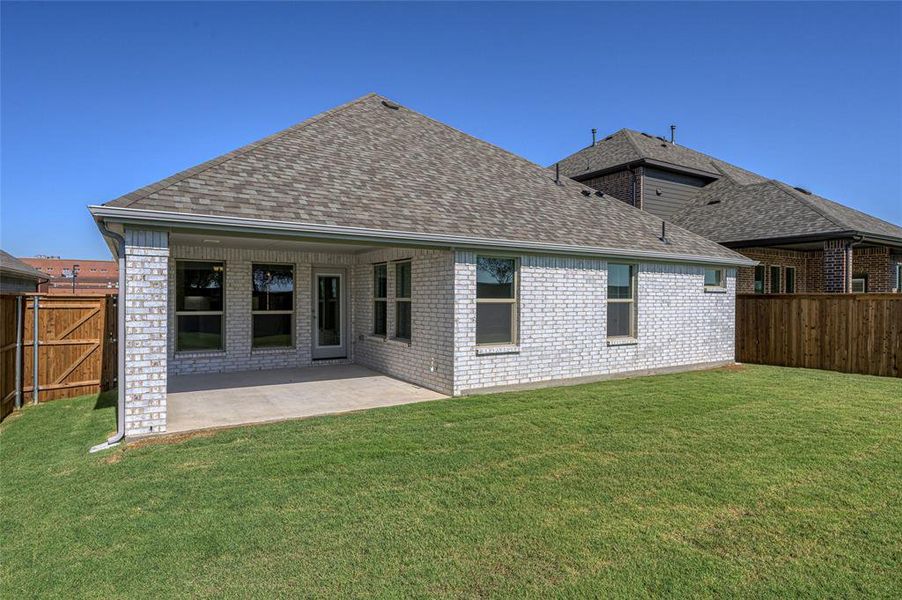 Rear view of house with a shingled roof, brick siding, a patio area, and a fenced backyard
